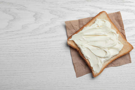 Slice of bread with tasty cream cheese on white wooden table, top view. Space for textの写真素材