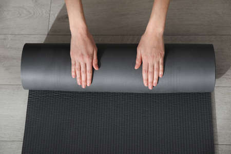 Top view of woman rolling yoga mat on floor