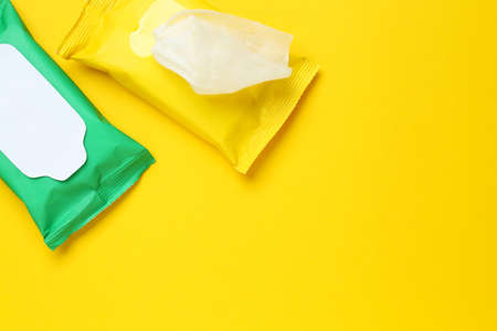 Wet wipes flow packs on yellow background, flat lay. Space for text
