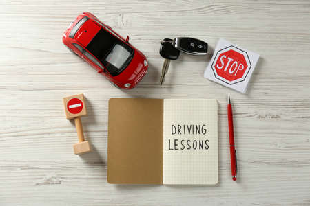 Flat lay composition with workbook for driving lessons and road signs on white wooden background. Passing license examの写真素材