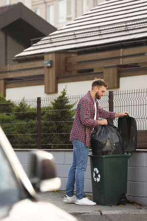 Man putting garbage bag into recycling bin outdoorsの写真素材
