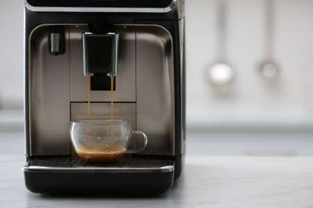 Modern electric espresso machine making coffee on white marble countertop in kitchenの写真素材