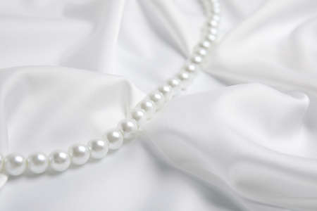 Beautiful pearls on white silk, closeup viewの写真素材