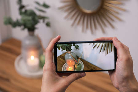 Woman taking photo of stylish interior accessories on wooden table with smartphone, closeupの写真素材