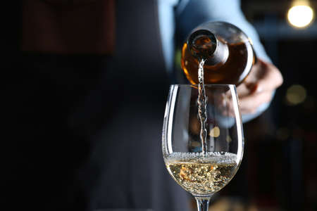 Bartender pouring white wine from bottle into glass indoors, closeup. Space for textの写真素材