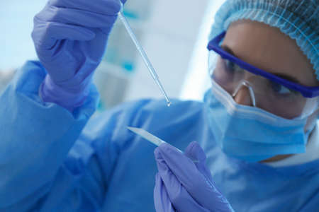 Scientist dripping sample onto glass slide in laboratory, focus on hands. medical research