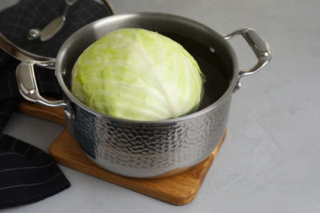 Sauce pan with hot water and cabbage for preparing stuffed rolls on light gray tableの写真素材
