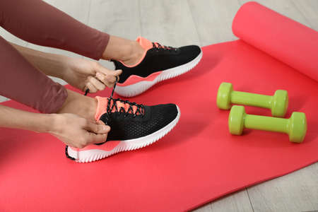 Woman tying sneaker's shoelaces on exercise mat, closeup