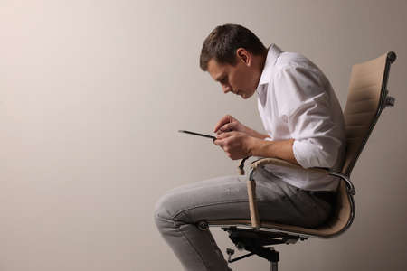 Man with bad posture using tablet while sitting on chair against gray background. Space for text