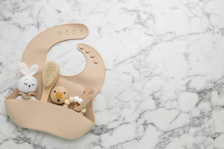 Flat lay composition with silicone baby bib, toys and accessories on white marble background. Space for textの写真素材