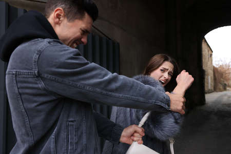 Thief trying to steal woman's bag in alley. Self defense conceptの写真素材