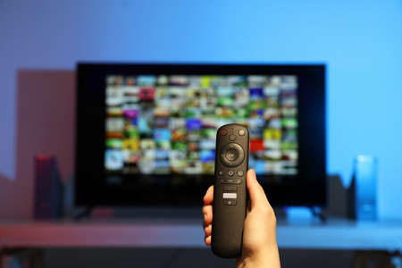 Woman switching channels on TV set with remote control at home, closeupの写真素材