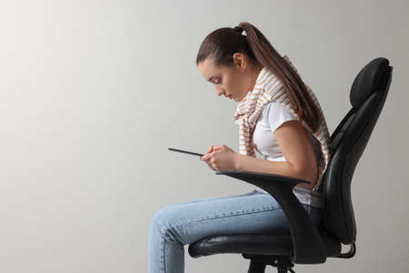 Young woman with poor posture using tablet while sitting on chair against gray background, space for textの写真素材
