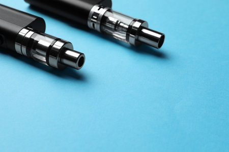 Two electronic cigarettes on light blue background, closeup. Space for textの写真素材