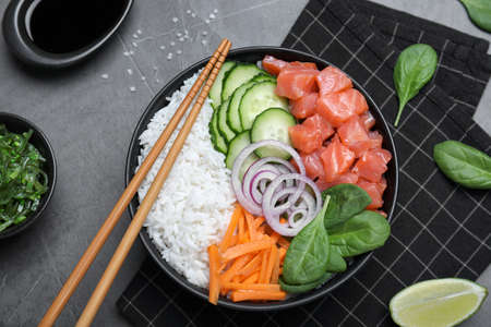 Delicious poke bowl with salmon and vegetables served on gray table, flat lay