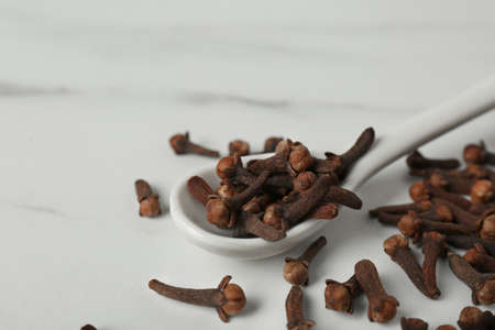 Aromatic dry cloves and ceramic spoon on white marble table, closeup