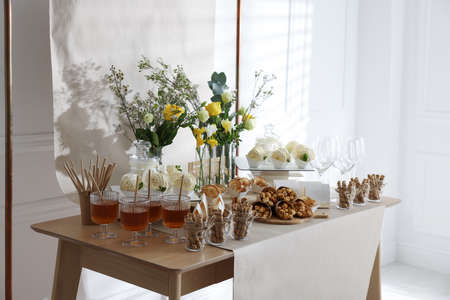 Delicious treats and glasses of drink on wooden table in room. sweet buffetの写真素材