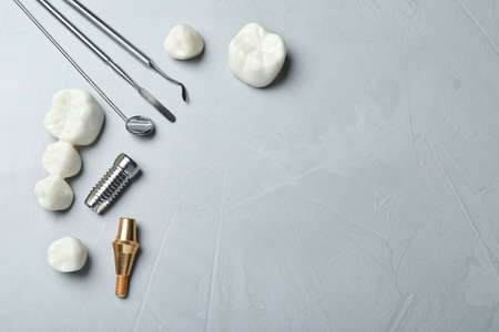 Post, abutment and different crowns of dental implant near medical tools on gray background, flat...