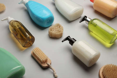 Many bottles of liquid soap, brushes and luffa on gray background