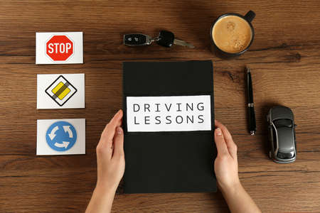 Woman with workbook for driving lessons and cup of coffee at wooden table, top view. Passing license examの写真素材