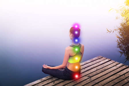 Woman meditating on wooden pier near river. Scheme of seven chakras, illustrationの写真素材