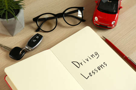 Workbook for driving lessons with pen and toy car on white wooden table. Passing license exam