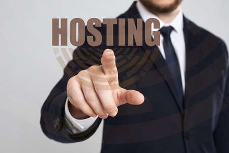 Businessman pointing at word HOSTING on virtual screen against light background, focus on handの写真素材