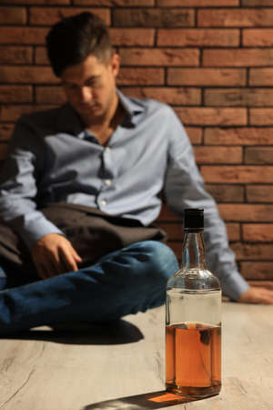 Addicted man sitting near red brick wall, focus on bottle of alcoholic drinkの写真素材