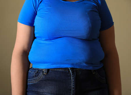 Overweight woman in tight t-shirt on light brown background, closeupの写真素材