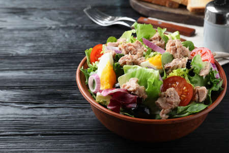 Bowl of delicious salad with canned tuna and vegetables on black wooden table, space for textの写真素材