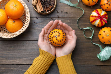 Woman holding pomander ball made of tangerine with cloves at wooden table, top viewの写真素材