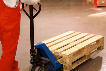 Worker moving wooden pallets with manual forklift in warehouse, closeup