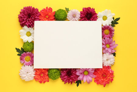 Frame made of beautiful chrysanthemum flowers and blank card on yellow background, flat lay. Space for textの写真素材