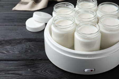 Modern yogurt maker with full jars on black wooden table. Space for textの写真素材