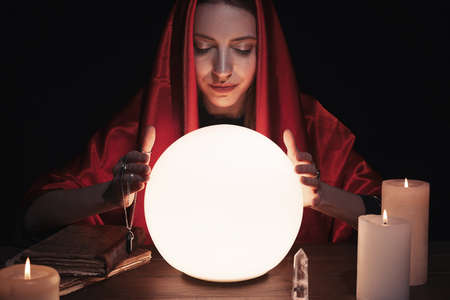 Soothsayer using glowing crystal ball to predict future at table in darkness. Fortune tellingの写真素材