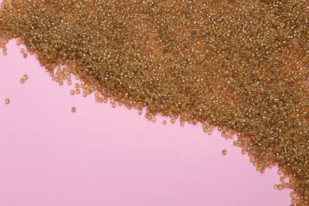Bright golden glass beads on pink background, flat lay. Space for text