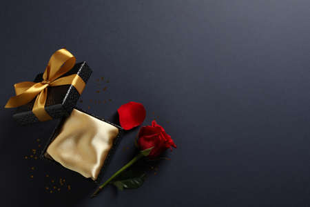 Open gift box and red rose on black background, flat lay. Space for textの写真素材