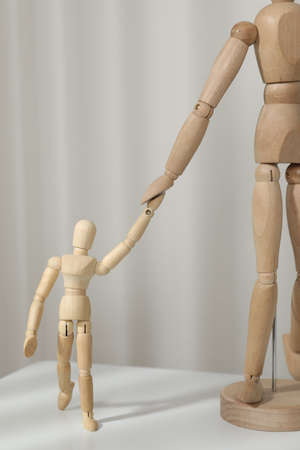 Wooden mannequins of parent with child on white table against light background. family day