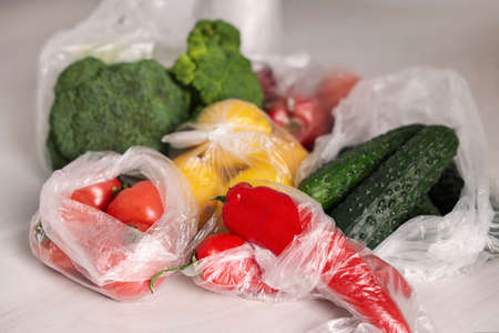 Plastic bags and fresh products on white table, closeup