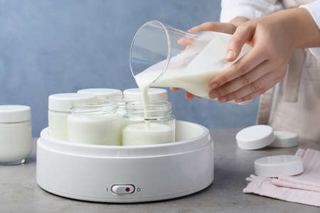 Woman pouring milk into glass jar at gray table, closeup. Making yogurtの写真素材