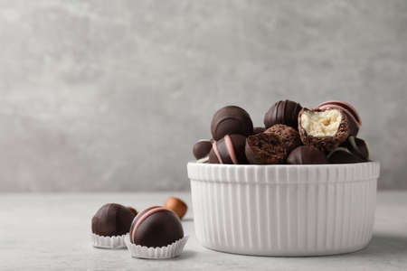 Different delicious chocolate truffles in a bowl on a light gray table. Space for text