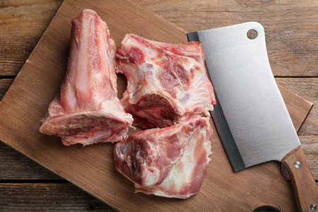 Cutting board with raw chopped meaty bones and butcher knife on wooden table, top viewの写真素材