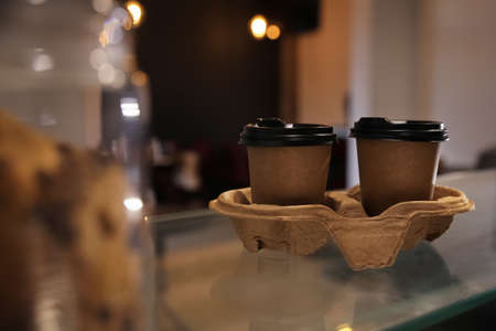 Takeaway coffee cups with cardboard holder on glass table in cafeの写真素材