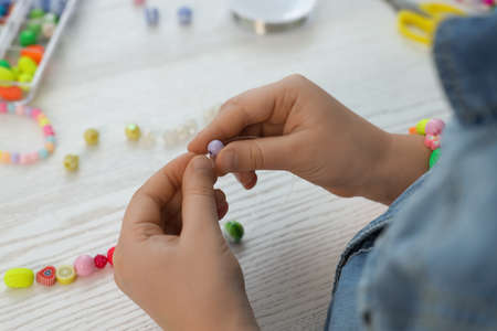 Little girl making beaded jewelry at white wooden table, closeupの写真素材