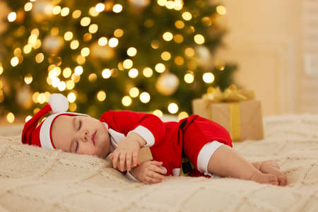 Cute baby in Christmas costume sleeping on knitted blanket against blurred festive lights. Winter holidayの写真素材