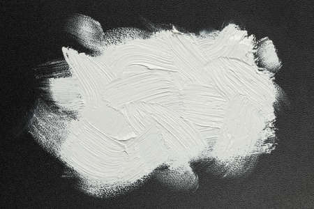 Strokes of white oil paint on black canvas, top view
