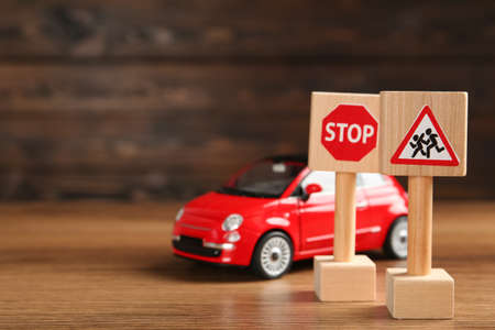 Miniature road signs and car on wooden table, space for text. driving school