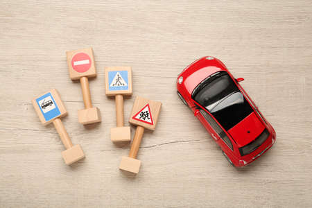 Different miniature road signs and car on wooden table, flat lay. driving school