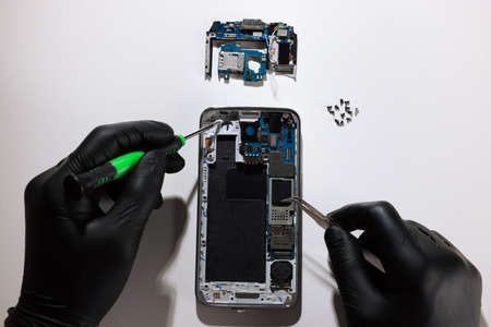 Technician repairing broken smartphone at white table, top view