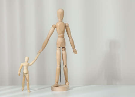 Wooden mannequins of parent with child on white table against light background, space for text....